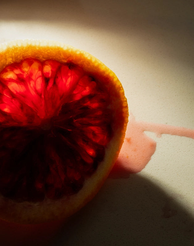 Blood orange slice submerged in golden light, referencing one of the natural ingredients in Looking for Each Other’s citrus-forward scent, Blinding Reflection from Tower Window.