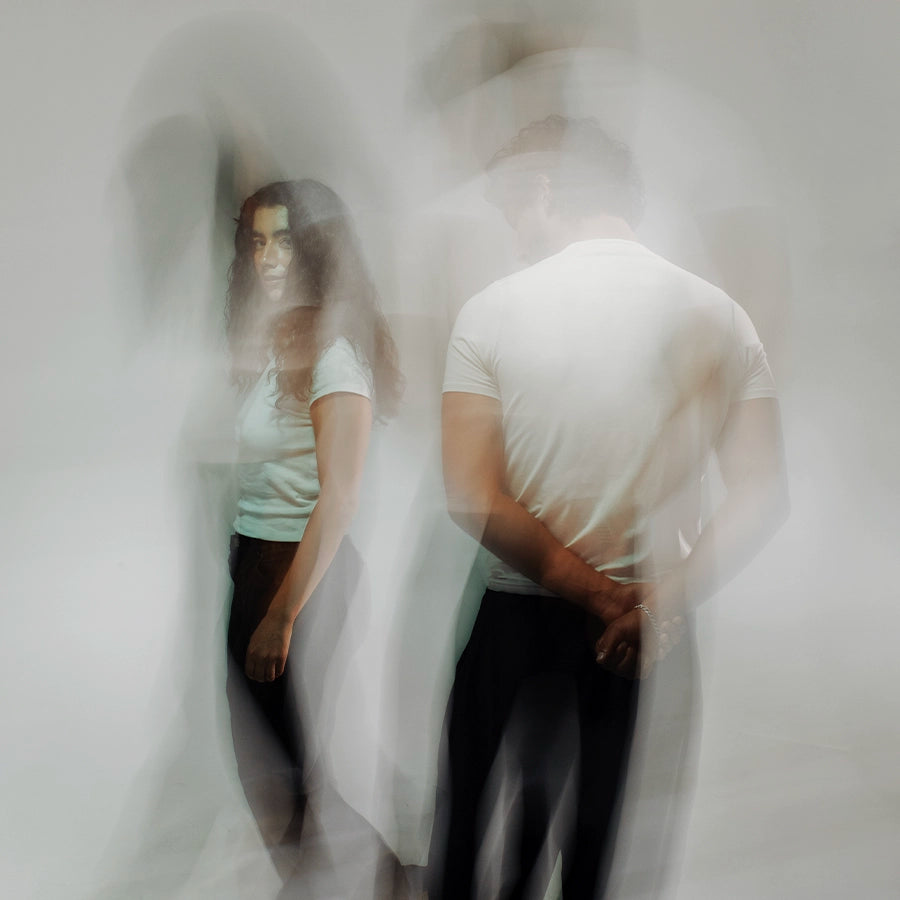 Two people—one facing forward, the other turned away—captured in soft motion blur against a white background. A ghostlike, layered image evoking emotional distance, longing, and the ephemeral nature of connection, in tune with Looking for Each Other’s poetic fragrance storytelling.