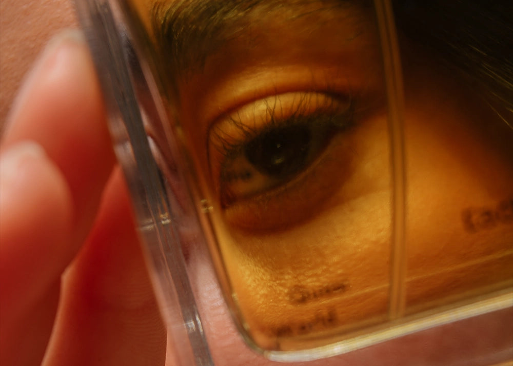 Close-up of an eye partially obscured by a perfume bottle from Looking for Each Other—highlighting the intimacy, reflection, and transparency behind the brand’s 100% botanical fragrances.