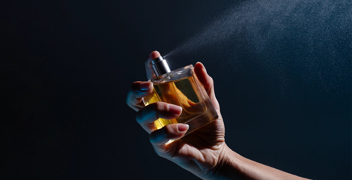 Hand holding a 50ml glass bottle of Looking for Each Other fragrance against a deep blue background. Represents the brand’s clean base of certified organic grape alcohol—used instead of synthetic ethanol.
