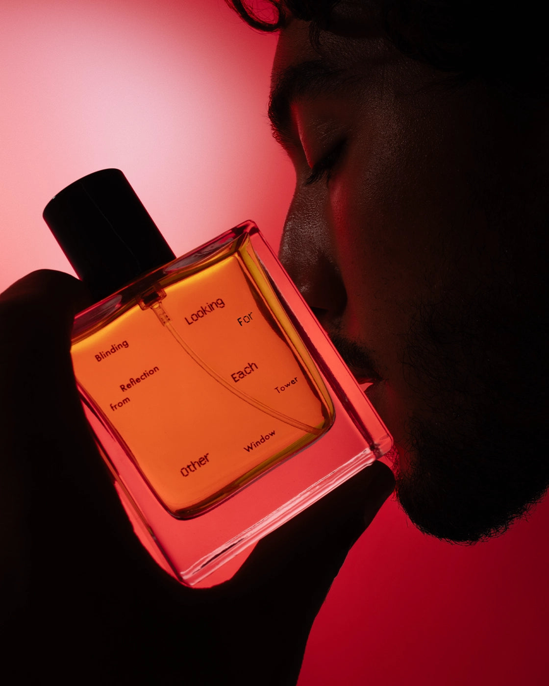A person holds and gently presses a bottle of Blinding Reflection from Tower Window by Looking for Each Other to their face, eyes closed in quiet connection. The glowing amber fragrance is bathed in red light, symbolizing the intimacy and radiance of this 100% botanical scent.