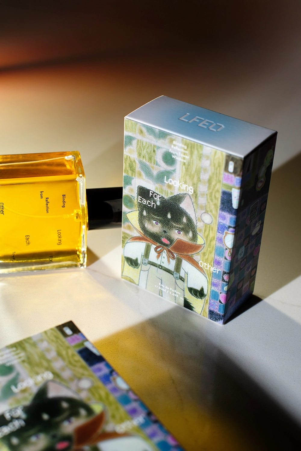 A bottle of Blinding Reflection from Tower Window by Looking for Each Other lies beside its illustrated outer box, featuring original artwork by Shee Liu. The whimsical, feline-inspired design contrasts with the minimal, glass bottle—showcasing the brand’s commitment to poetic storytelling and 100% botanical fragrance.